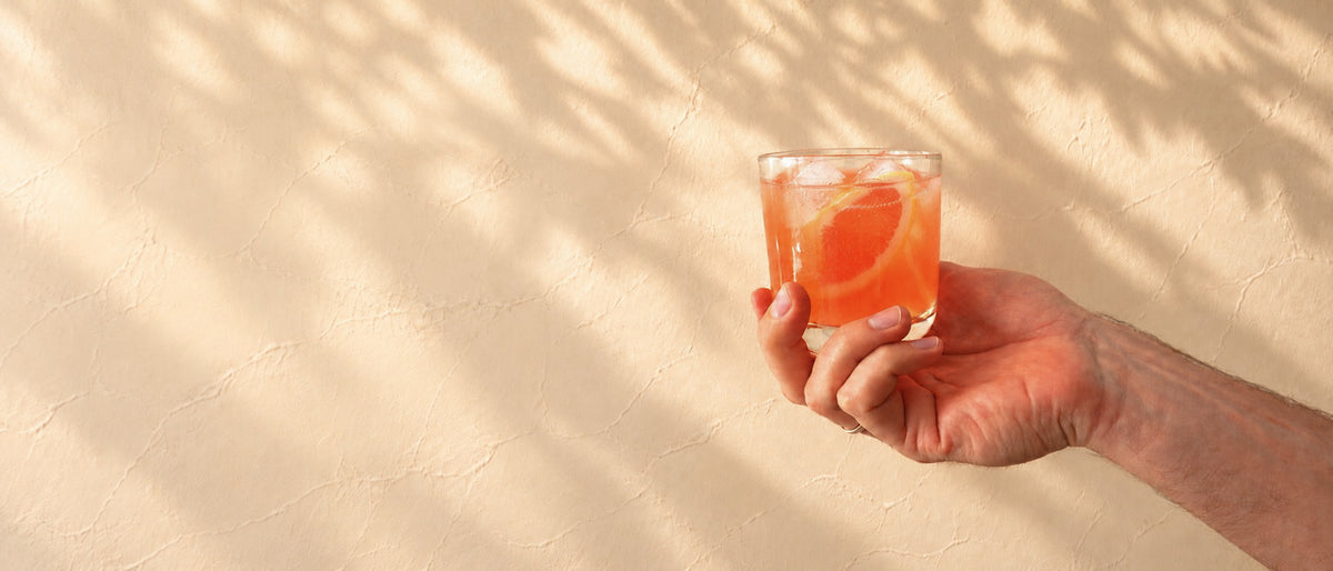 ROUTINE8 Longevity Komplex Nahrungsergänzungsmittel als Blutorangen-Getränk im Glas vor heller Wand.
